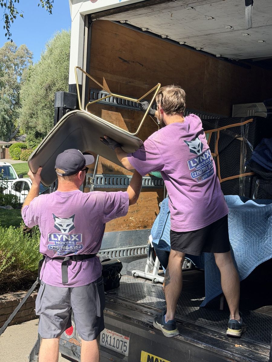 Two Lynx Movers crew members lifting furniture into the truck together