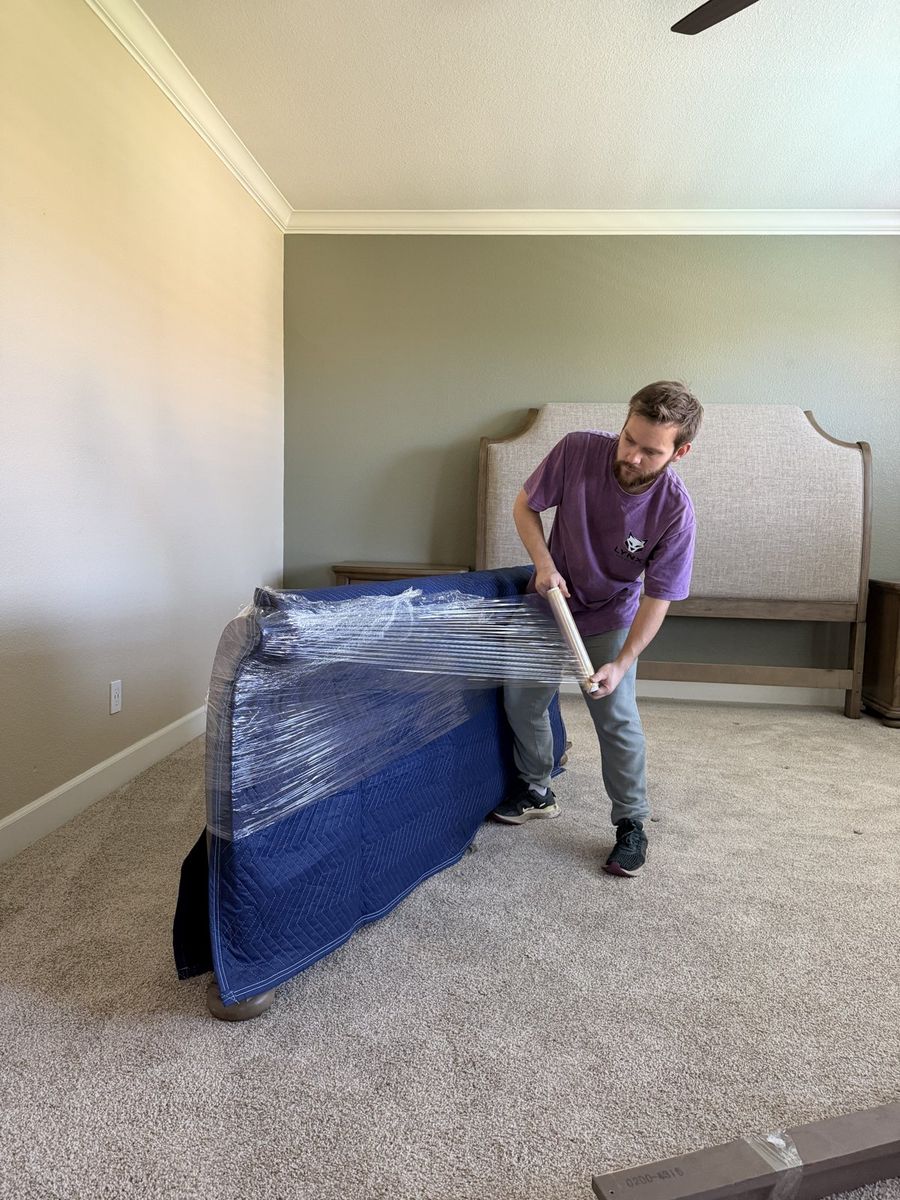 A Lynx Movers crew member wrapping furniture in a moving blanket inside a home